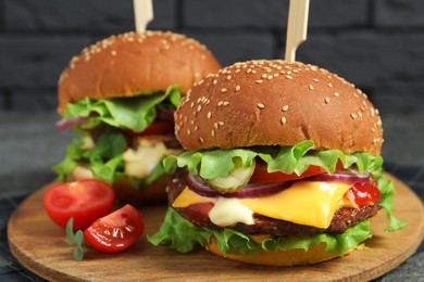Photo of Delicious burgers with beef patty and tomatoes on wooden board, closeup
