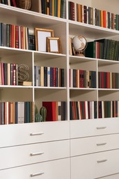 Photo of Collection of different books and decorative elements on shelves in home library