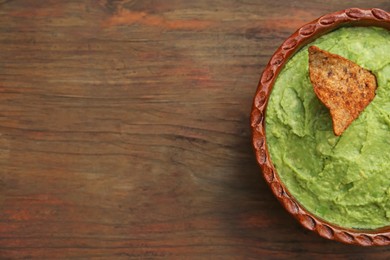 Photo of Delicious guacamole made of avocados and nachos on wooden table, top view. Space for text