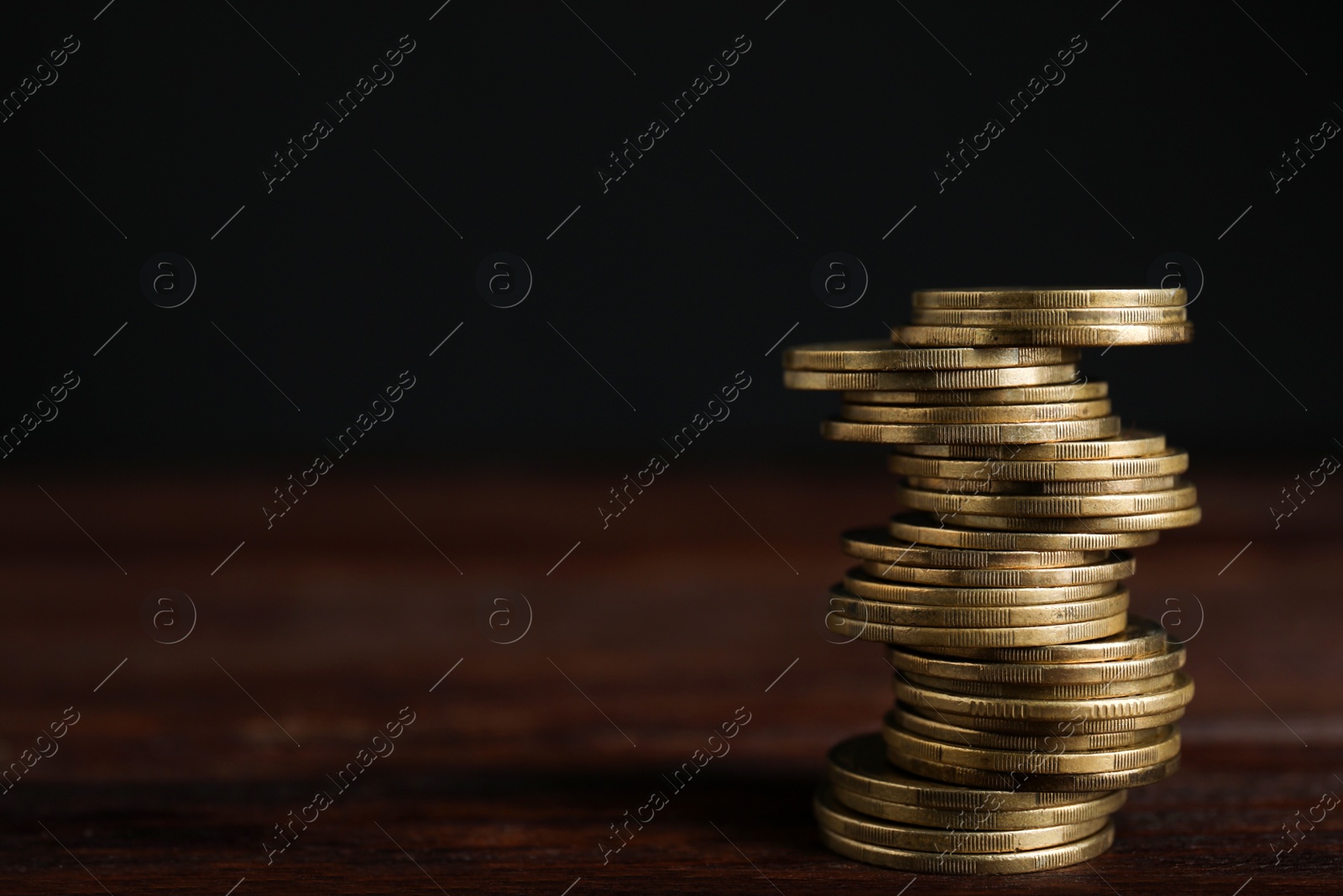 Photo of Many coins stacked on wooden table against black background, space for text