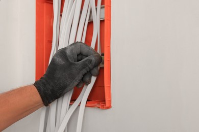 Photo of Electrician installing switchboard indoors, closeup with space for text. Installation of electrical wiring