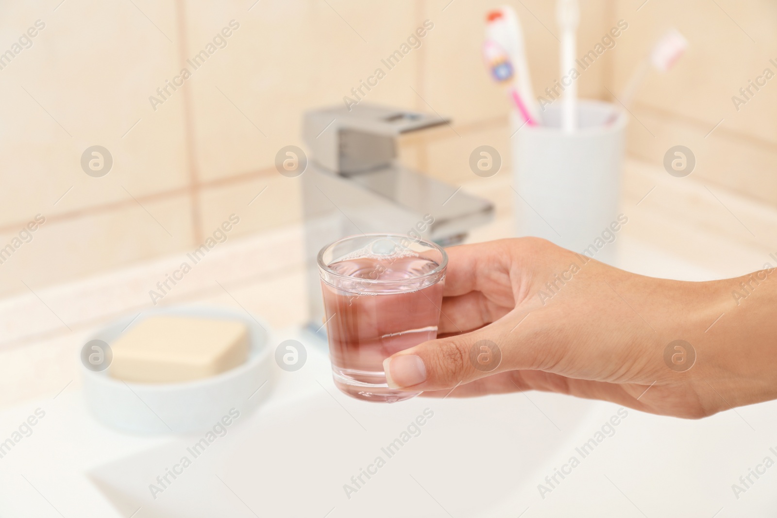 Photo of Woman holding glass with mouthwash for teeth and oral care in bathroom