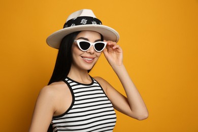 Fashionable young woman in stylish outfit with bandana on orange background