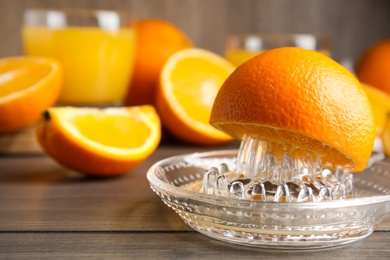 Fresh ripe oranges and glass squeezer on wooden table, closeup. Space for text