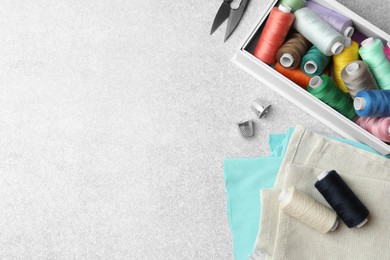 Flat lay composition with spools of threads and sewing tools on light background, space for text