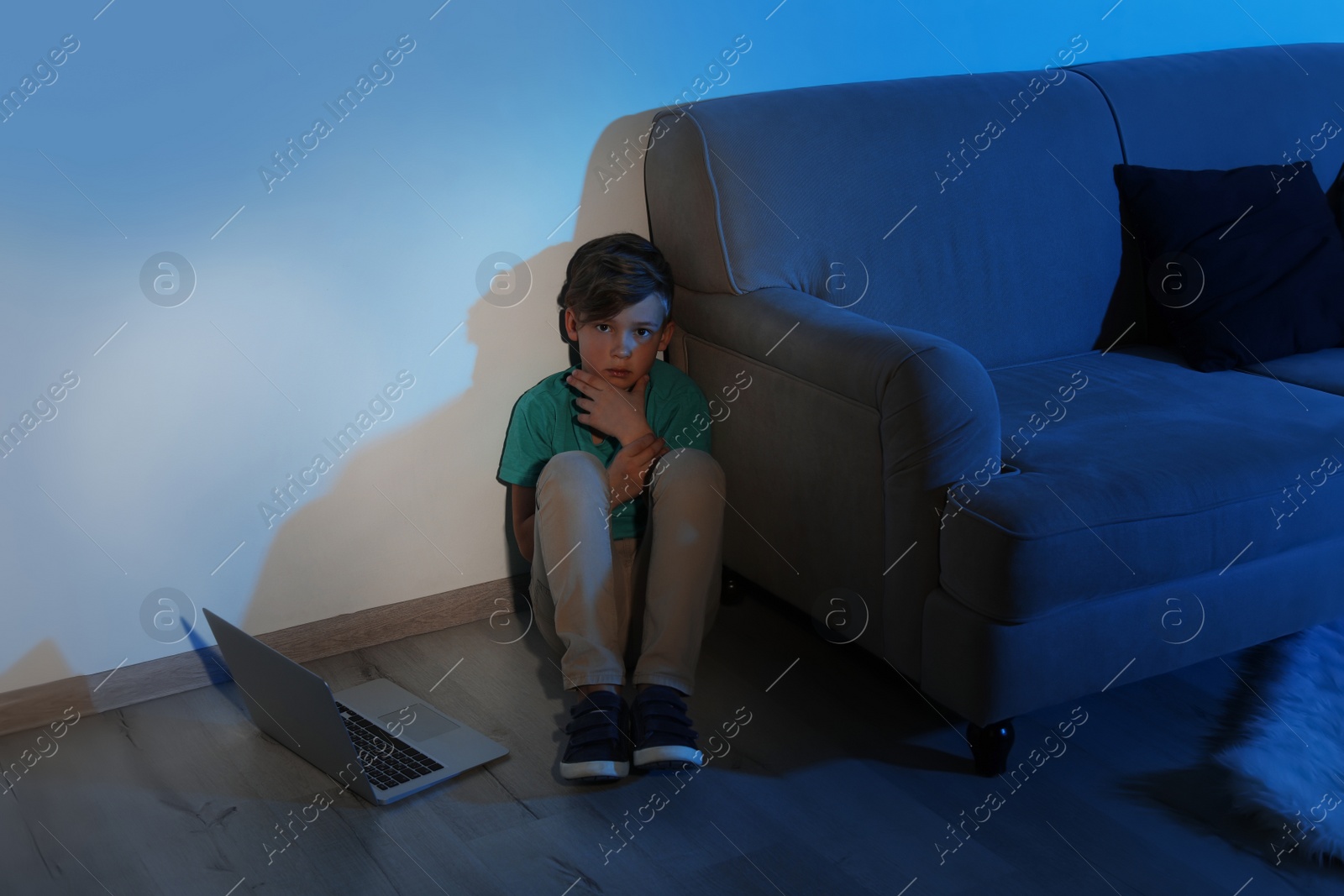 Photo of Frightened little child with laptop on floor in dark room. Danger of internet