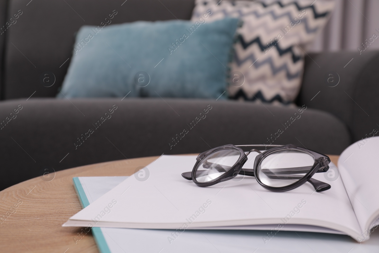 Photo of Glasses and notebooks on wooden table near sofa in room, closeup