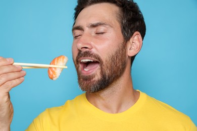 Handsome man eating sushi with chopsticks on light blue background, closeup