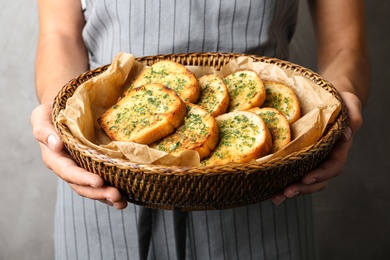 Woman holding slices of toasted bread with garlic and herbs against grey background, closeup