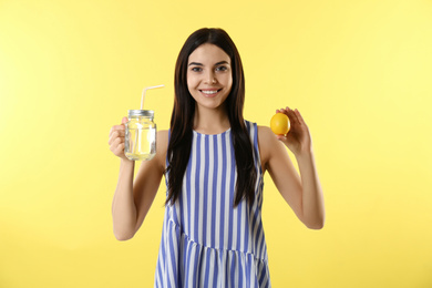 Photo of Beautiful young woman with tasty lemon water and fresh fruit on yellow background