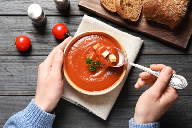 Photo of Woman eating fresh homemade tomato soup at wooden table, top view