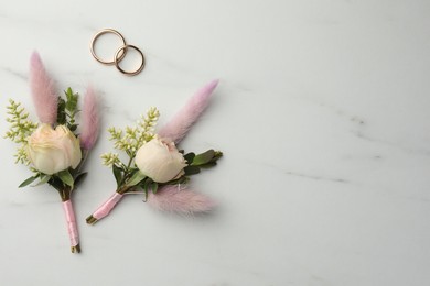 Photo of Small stylish boutonnieres and rings on white marble table, flat lay. Space for text