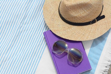 Beach towel with book, sunglasses and straw hat on sand, flat lay. Space for text