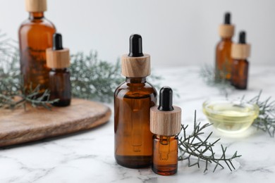 Photo of Bottles of juniper essential oil and twigs on white marble table