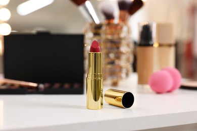 Photo of Red lipstick and other cosmetic products on white table in makeup room, selective focus