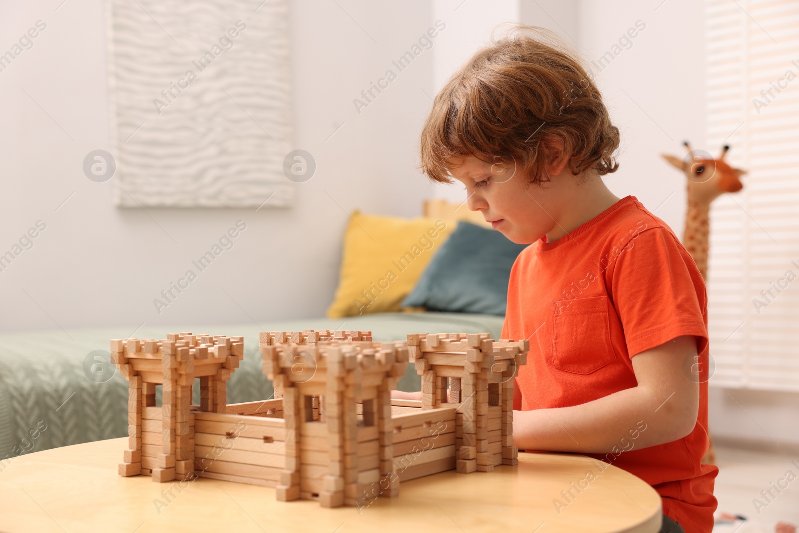 Photo of Cute little boy playing with wooden fortress at table in room. Child's toy