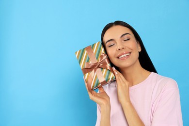 Happy young woman holding gift box on light blue background