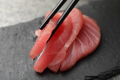 Photo of Taking tasty sashimi (piece of fresh raw tuna) from black board, closeup