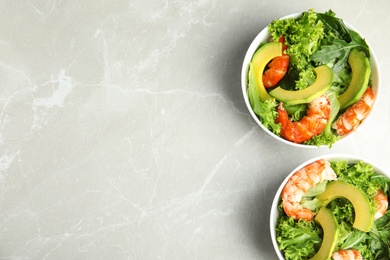 Photo of Delicious avocado salad with shrimps in bowls on grey marble table, flat lay. Space for text