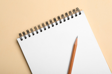 Photo of Open notebook and pencil on beige background, top view