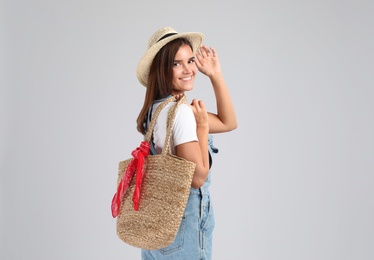 Young woman with stylish straw bag on light grey background
