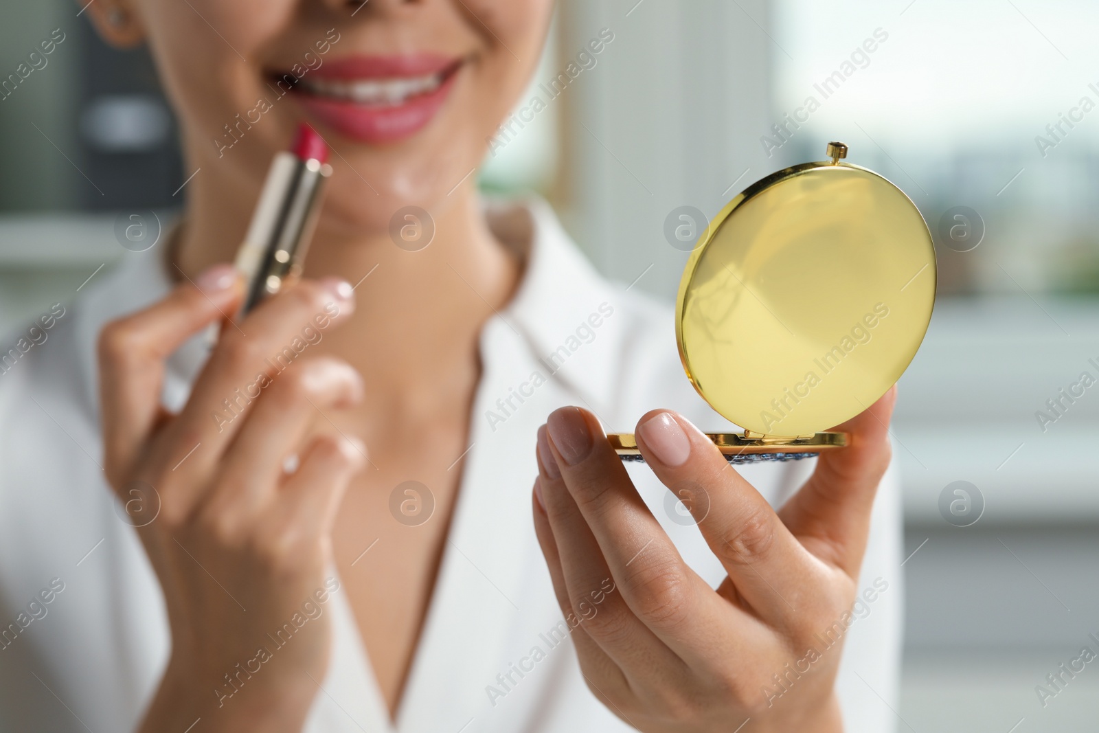 Photo of Young woman using cosmetic pocket mirror while applying make up indoors, closeup