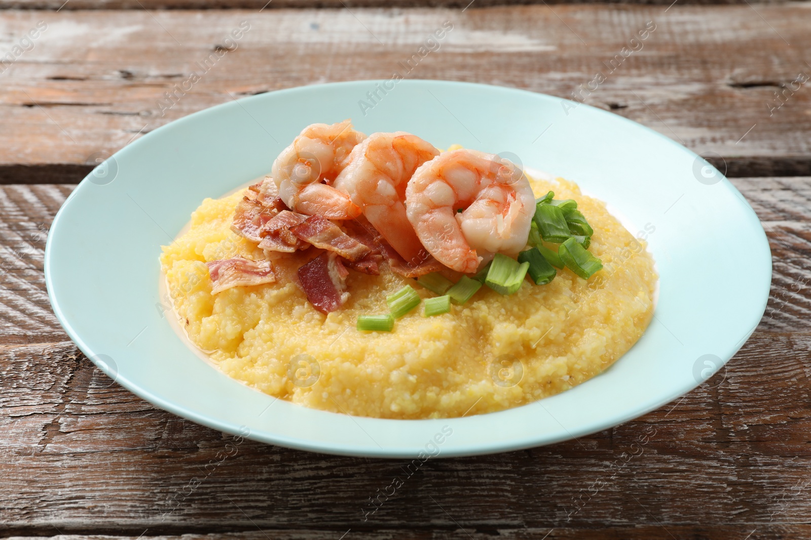 Photo of Plate with fresh tasty shrimps, bacon, grits and green onion on wooden table