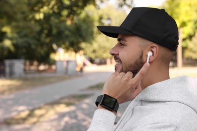 Photo of Young man with wireless headphones listening to music in park. Space for text