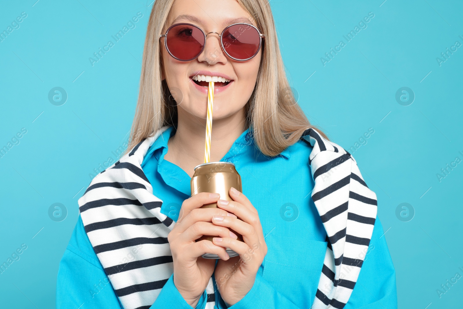 Photo of Beautiful happy woman drinking from beverage can on light blue background