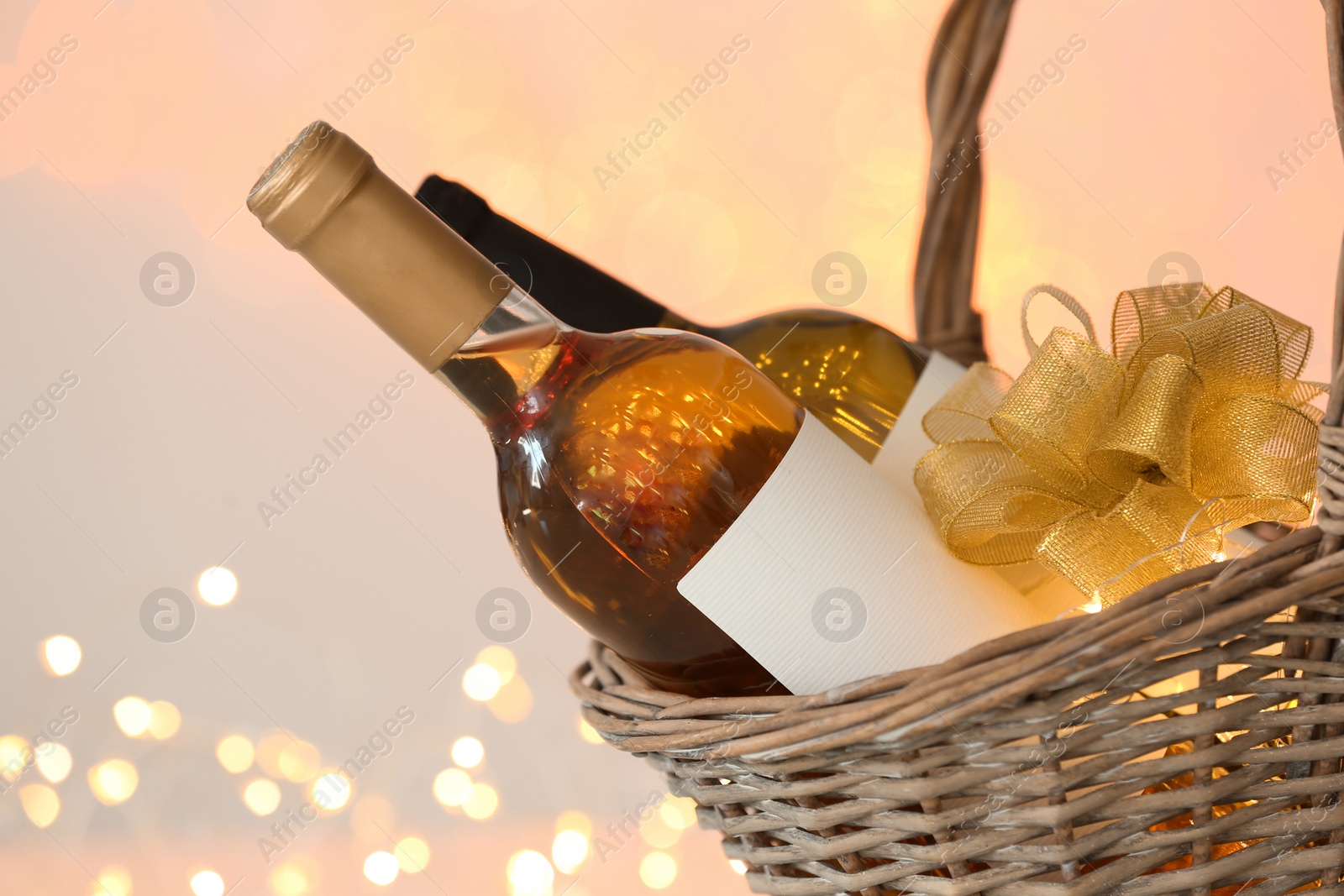 Photo of Wicker basket with bottles of wine against blurred background, closeup