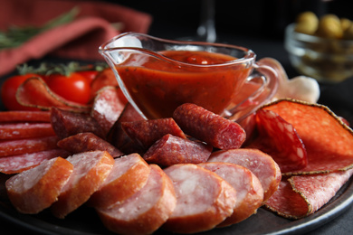 Different types of sausages with sauce served on black table, closeup