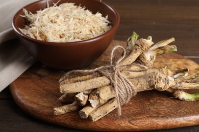 Photo of Grated horseradish and roots on wooden table, closeup