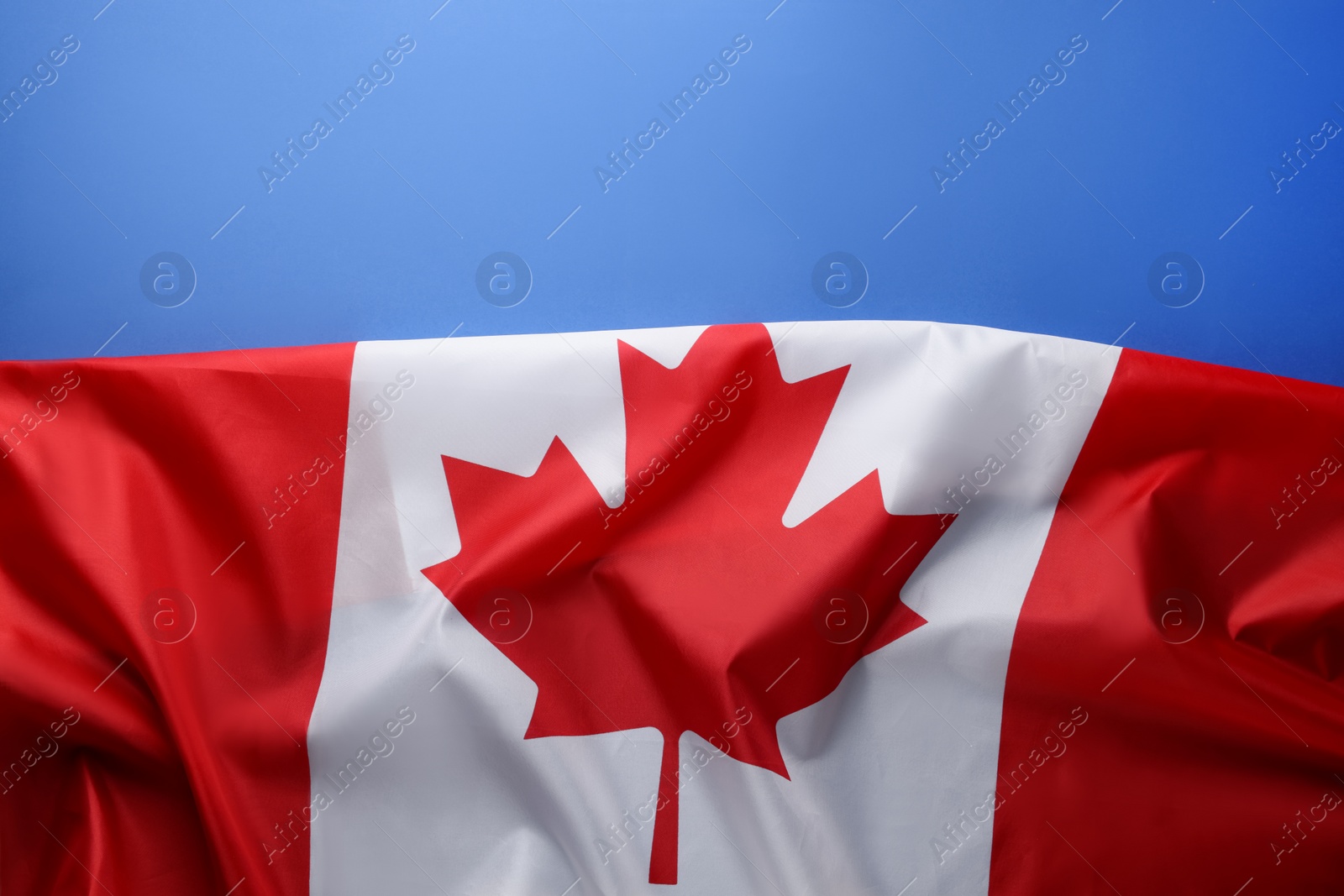 Photo of Flag of Canada on blue background, top view. Space for text