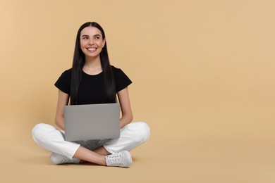 Happy woman with laptop sitting on beige background, space for text