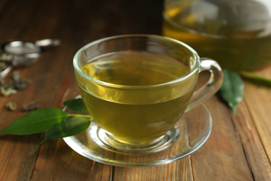 Photo of Cup of aromatic green tea and leaves on wooden table