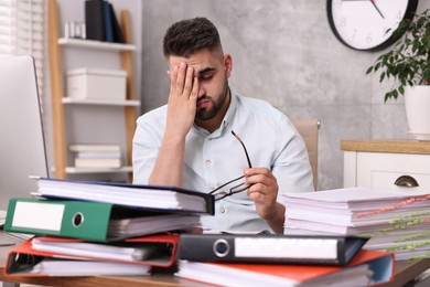 Photo of Overwhelmed man surrounded by documents at workplace in office
