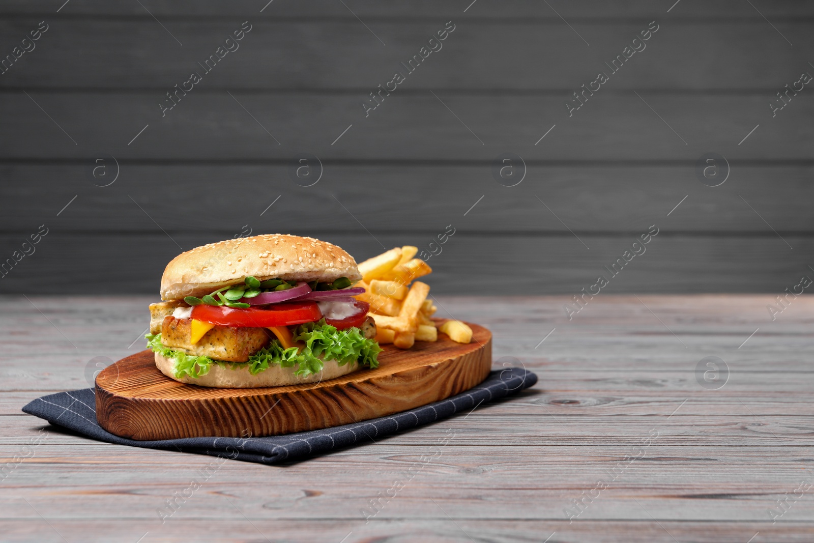 Photo of Delicious tofu burger served with french fries on grey wooden table. Space for text