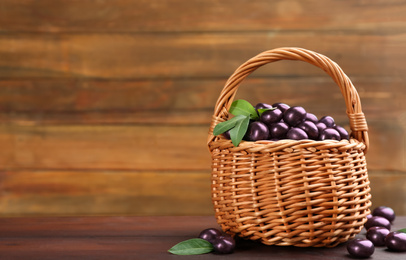 Photo of Basket and tasty acai berries on wooden table. Space for text