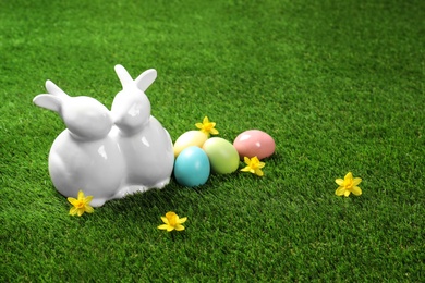 Ceramic Easter bunnies and dyed eggs on green grass, space for text