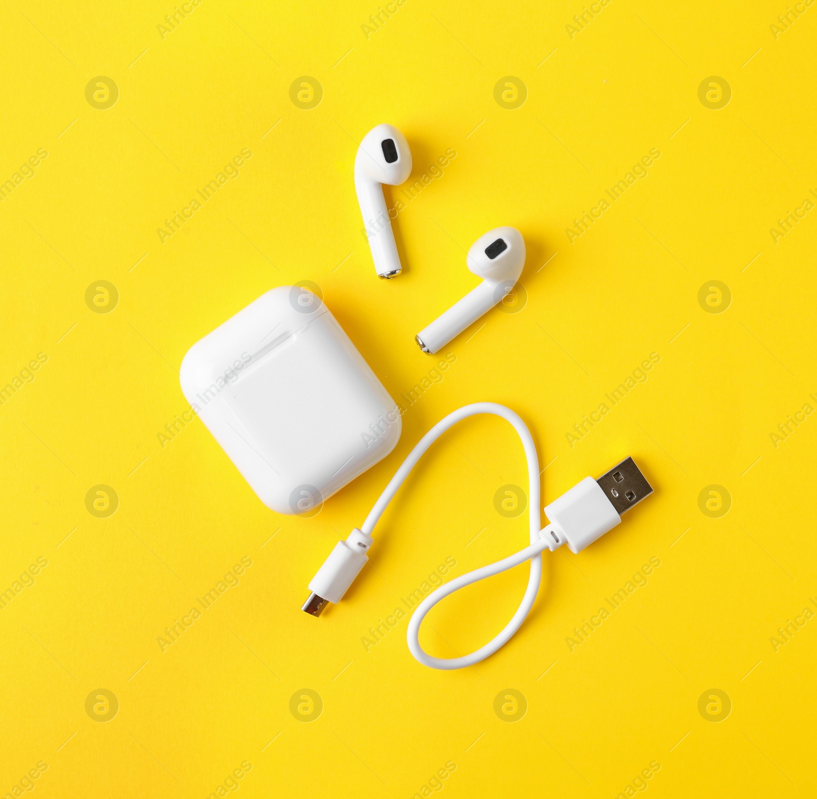 Photo of Modern wireless earphones and charging case with cable on yellow background, flat lay