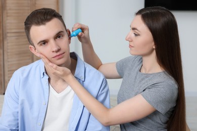 Woman dripping medication into man's ear at home