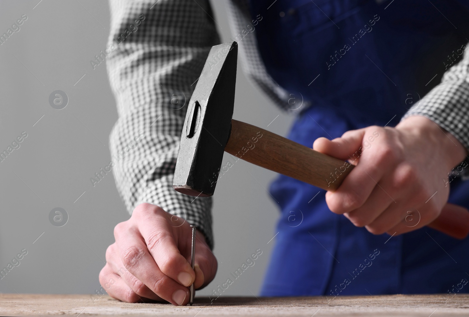 Photo of Professional repairman hammering nail into wooden board indoors, closeup