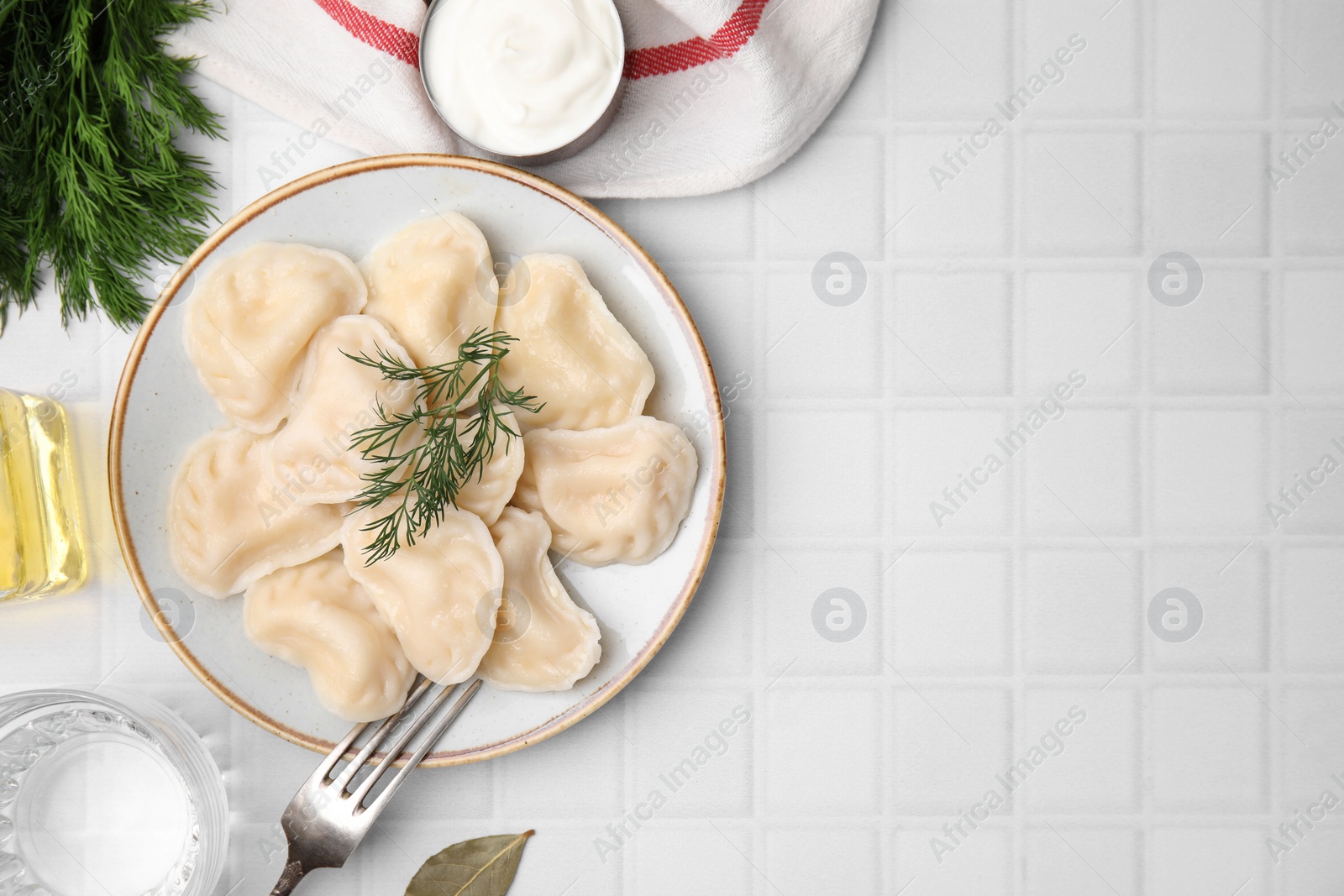 Photo of Cooked dumplings (varenyky) with tasty filling and sour cream on white tiled table, flat lay. Space for text