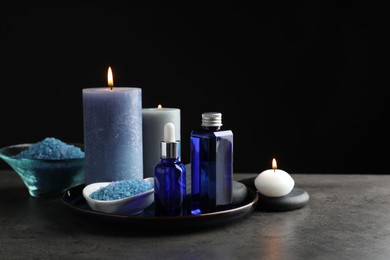 Photo of Spa composition. Cosmetic products, burning candles and sea salt on gray table against black background, space for text