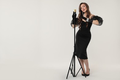 Photo of Beautiful young woman in stylish dress with microphone singing on light grey background, space for text