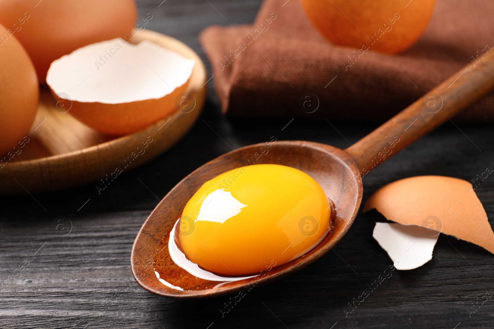 Photo of Spoon with raw egg yolk on black wooden table, closeup