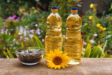 Photo of Bottles of cooking oil with sunflower and seeds on wooden table outdoors