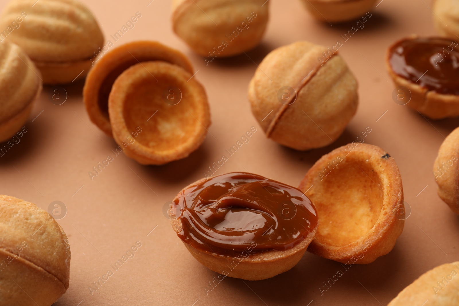 Photo of Homemade walnut shaped cookies with boiled condensed milk on pale brown background, closeup