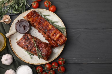 Photo of Tasty roasted pork ribs served with sauce, tomatoes and other products on grey wooden table, flat lay. Space for text