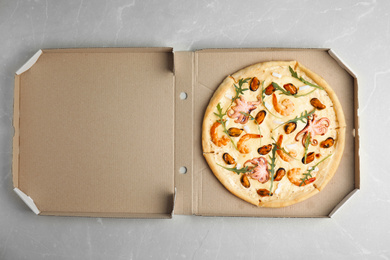 Photo of Delicious seafood pizza in cardboard box on grey marble table, top view